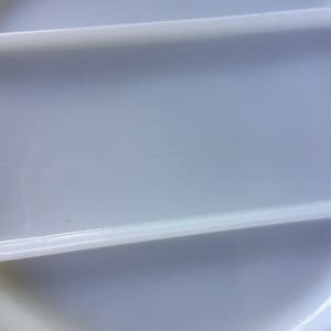 May include: A white plastic lid with two raised ridges. The lid is smooth and has a slight sheen.