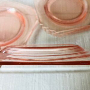 May include: A set of four pink glass plates with a scalloped edge. The plates are stacked on top of each other.