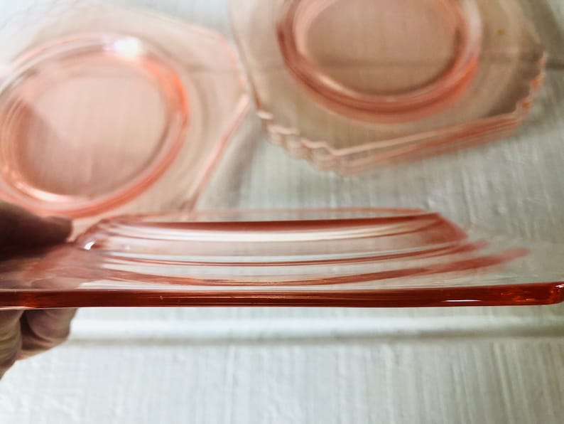 May include: A set of four pink glass plates with a scalloped edge. The plates are stacked on top of each other.