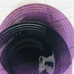May include: A set of purple and black dinner plates. The plates are stacked on top of each other, with the purple plate on the bottom and the black plate on top.