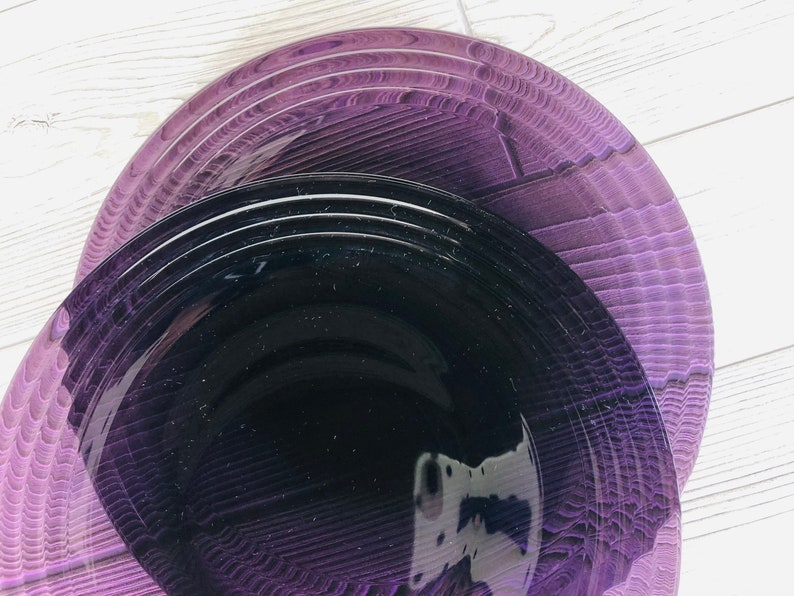May include: A set of purple and black dinner plates. The plates are stacked on top of each other, with the purple plate on the bottom and the black plate on top.