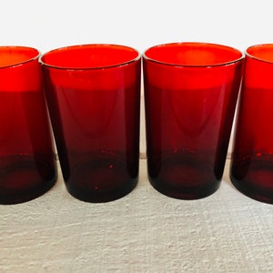 May include: Four red-tinted drinking glasses. The glasses have a cylindrical shape with a slightly tapered design. The rims of the glasses are a bright red, and the color fades to a darker red towards the base. The glasses are arranged in a row.