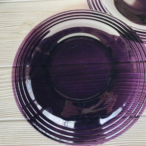 May include: A deep purple dinner plate with a glossy finish and a slightly raised rim. The plate has a subtle, striped pattern.