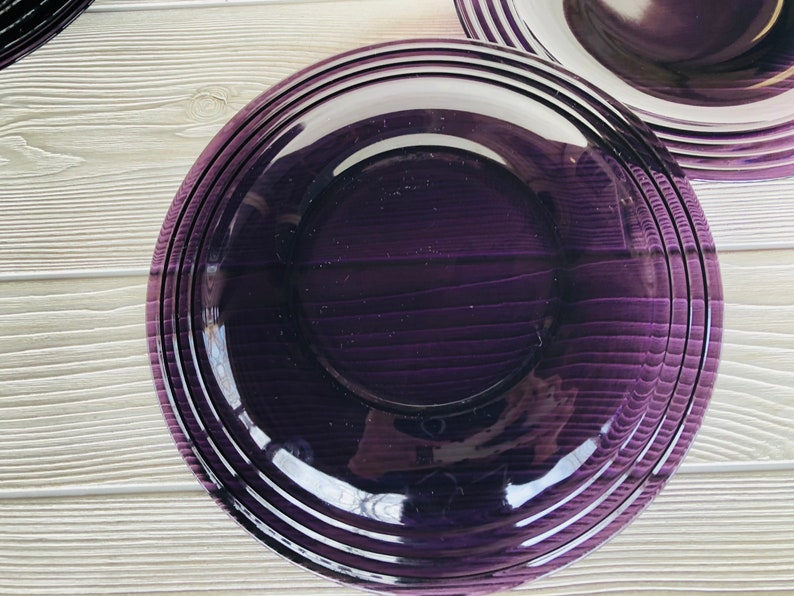 May include: A deep purple dinner plate with a glossy finish and a slightly raised rim. The plate has a subtle, striped pattern.