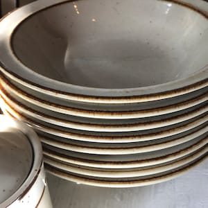 Może przedstawiać: Stos białych ceramicznych misek z brązowymi obw&oacute;dkami. Miski są włożone jedna w drugą i mają kropkowaną glazurę.