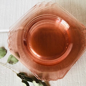 May include: A stack of pink glass dessert plates with scalloped edges. The plates are stacked on a white surface.