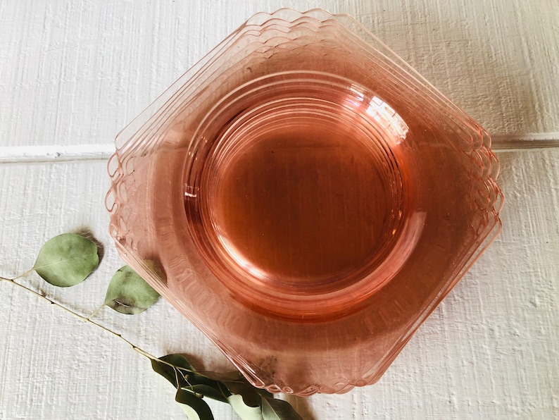 May include: A stack of pink glass dessert plates with scalloped edges. The plates are stacked on a white surface.