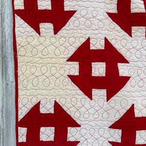 Peut inclure: Gros plan sur une courtepointe faite &agrave; la main avec un motif r&eacute;p&eacute;t&eacute; de formes rouges en forme de fl&egrave;che sur un fond blanc. La courtepointe a des coutures d&eacute;coratives rouges dans un motif en boucle continue. La courtepointe est probablement en coton ou en tissu similaire.