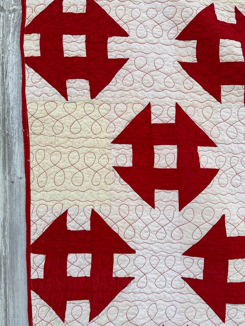 Peut inclure: Gros plan sur une courtepointe faite &agrave; la main avec un motif r&eacute;p&eacute;t&eacute; de formes rouges en forme de fl&egrave;che sur un fond blanc. La courtepointe a des coutures d&eacute;coratives rouges dans un motif en boucle continue. La courtepointe est probablement en coton ou en tissu similaire.