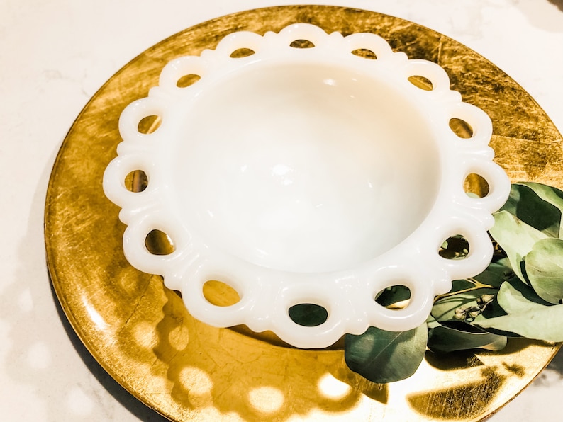 May include: A white milk glass bowl with a scalloped edge and a gold charger plate underneath.