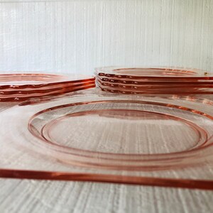 May include: A stack of six pink glass plates with scalloped edges. The plates are arranged in a pyramid shape, with the largest plate at the bottom and the smallest plate at the top.