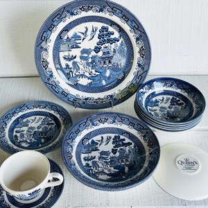 May include: A collection of blue and white Willow pattern china. The set includes plates, bowls, and a teacup with saucer. The designs feature a scenic landscape with pagodas, bridges, and birds. The plates and bowls have a decorative border.