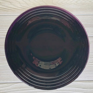 May include: A deep purple ceramic bowl with a smooth, glossy finish. The bowl has a wide, shallow shape with a slightly raised rim.