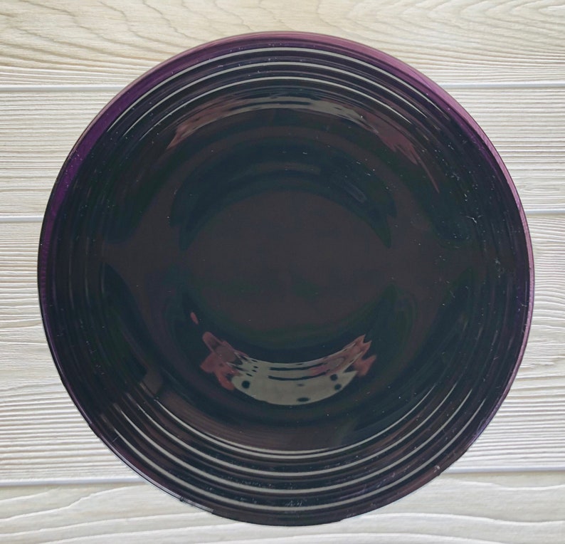 May include: A deep purple ceramic bowl with a smooth, glossy finish. The bowl has a wide, shallow shape with a slightly raised rim.