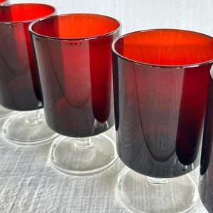 May include: A set of six stemmed glasses. The glasses have a deep red color that fades to a darker shade towards the base. The rims are a bright red. The stems and bases are clear glass.