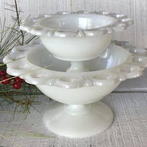 May include: A white milk glass pedestal bowl with a scalloped edge and a smaller bowl on top. The bowl has a scalloped edge and is perfect for serving snacks or desserts.