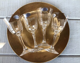 May include: Four clear glass wine glasses with a gold rim and a blue sticker that says "Toscana" on each glass. The glasses are on a gold charger.