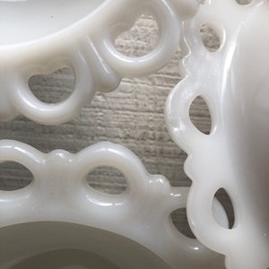 May include: Three white milk glass bowls with scalloped edges and openwork designs. The bowls are stacked on top of each other.