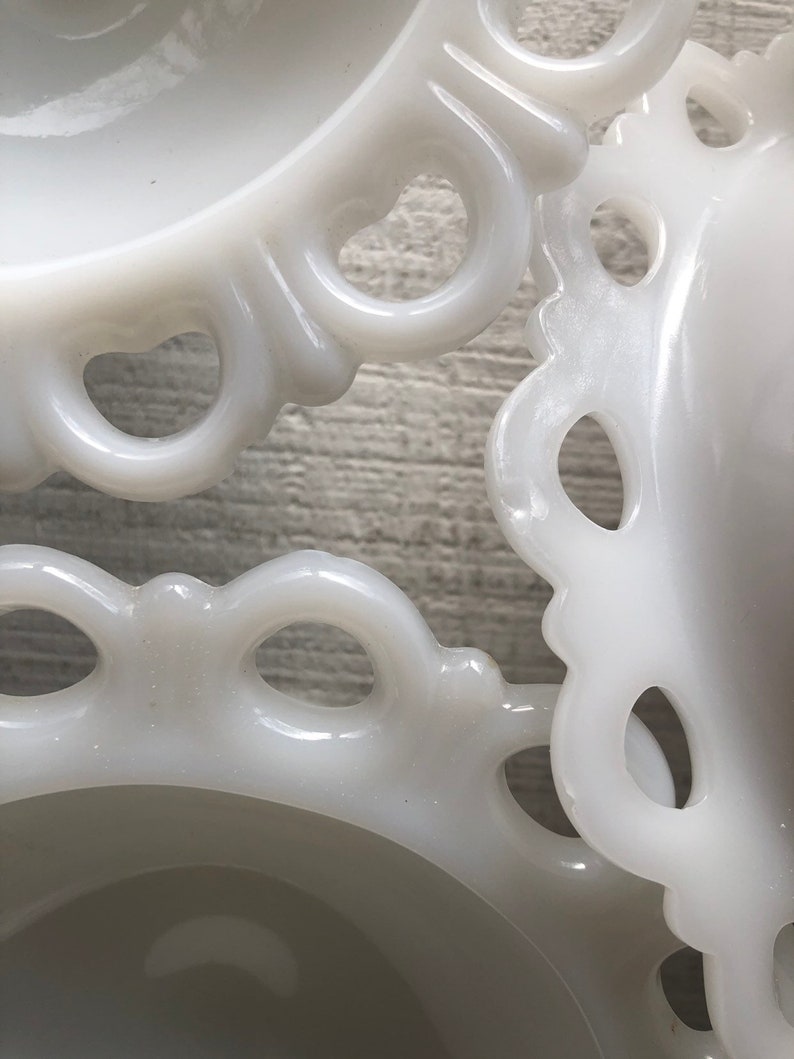 May include: Three white milk glass bowls with scalloped edges and openwork designs. The bowls are stacked on top of each other.