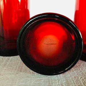 May include: A collection of red-tinted drinking glasses. The glasses have a dark red base that fades to a lighter red towards the top. The bottom of one glass is in focus, showing its dark rim and the interior.