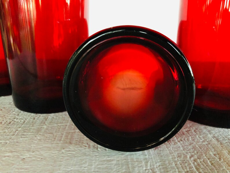 May include: A collection of red-tinted drinking glasses. The glasses have a dark red base that fades to a lighter red towards the top. The bottom of one glass is in focus, showing its dark rim and the interior.