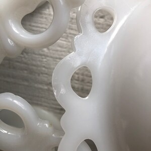 May include: Two white milk glass bowls with scalloped edges and openwork designs. The bowls are stacked on top of each other.