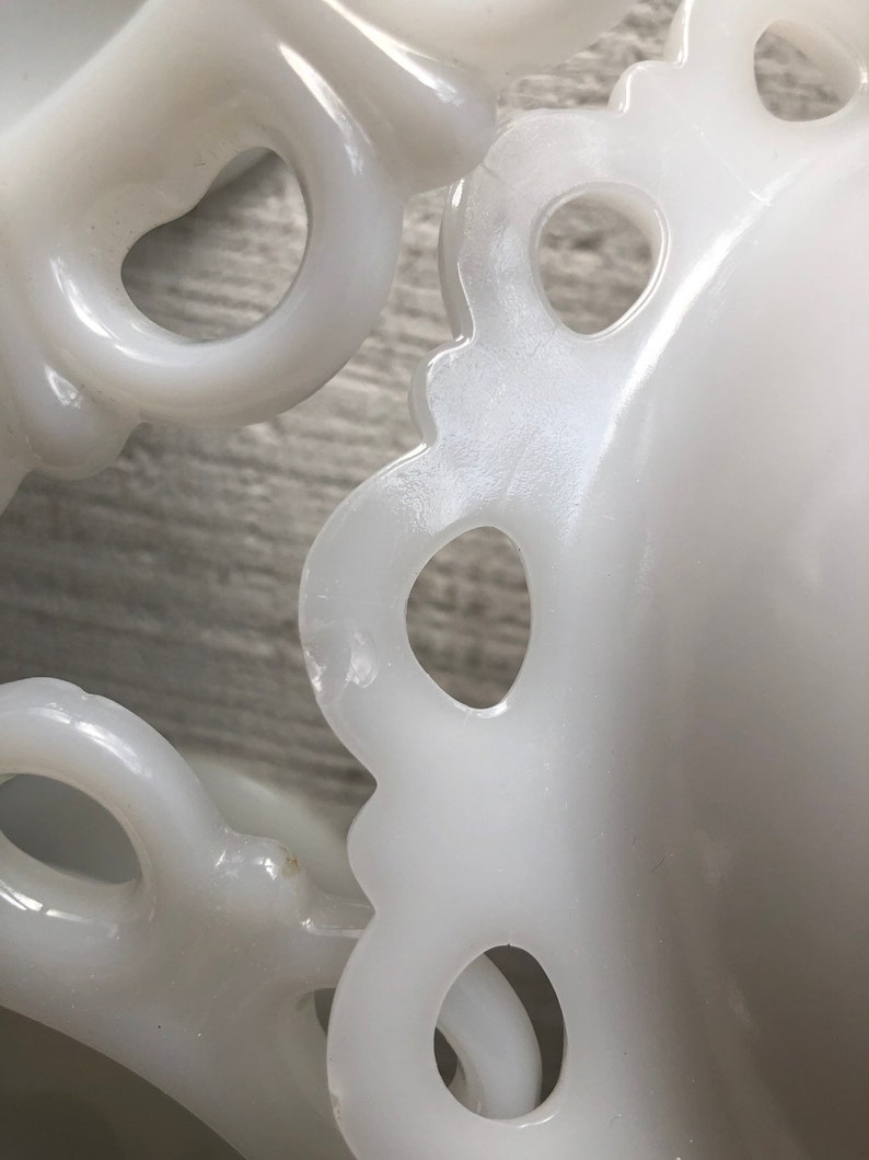 May include: Two white milk glass bowls with scalloped edges and openwork designs. The bowls are stacked on top of each other.