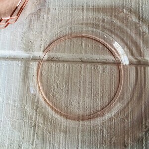 May include: A clear glass plate with a pink rim. The plate is on a white wooden surface.