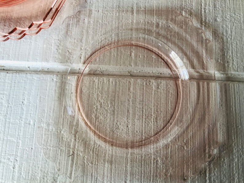May include: A clear glass plate with a pink rim. The plate is on a white wooden surface.