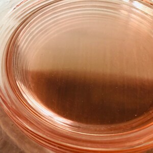 May include: A close-up of a pink glass plate with a concentric circle design. The plate is made of clear glass with a pink tint.