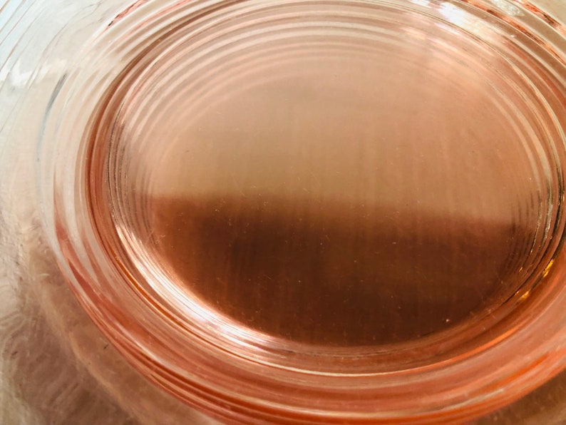 May include: A close-up of a pink glass plate with a concentric circle design. The plate is made of clear glass with a pink tint.
