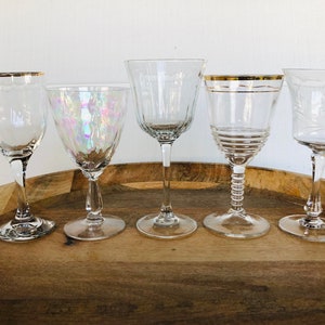 May include: Five clear glass wine glasses with gold rims on a wooden tray. The glasses have different designs and shapes.