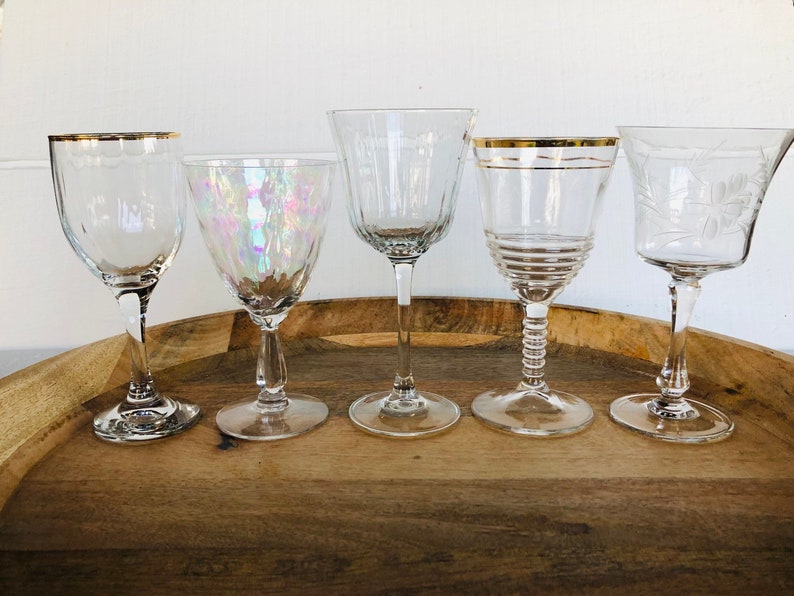 May include: Five clear glass wine glasses with gold rims on a wooden tray. The glasses have different designs and shapes.