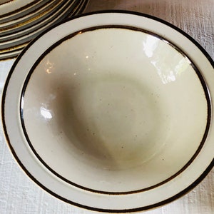 Może przedstawiać: Biała ceramiczna miska z brązową obw&oacute;dką. Miska ma lekko fakturowaną powierzchnię i idealnie nadaje się do serwowania zupy lub sałatki.