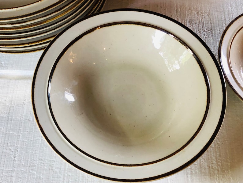 Może przedstawiać: Biała ceramiczna miska z brązową obw&oacute;dką. Miska ma lekko fakturowaną powierzchnię i idealnie nadaje się do serwowania zupy lub sałatki.