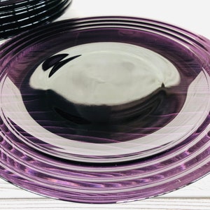 May include: A set of purple glass dinner plates with a concentric circle design. The plates are stacked on top of each other.