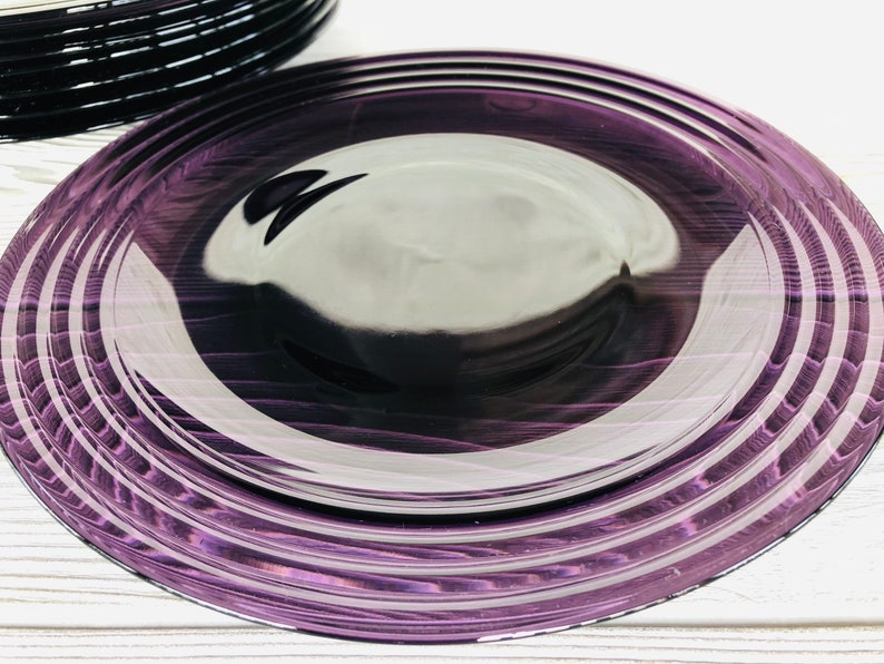 May include: A set of purple glass dinner plates with a concentric circle design. The plates are stacked on top of each other.