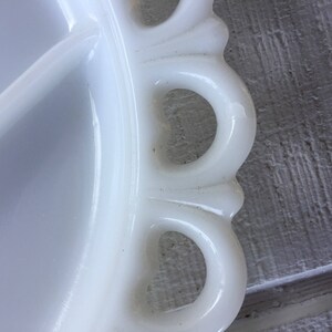 May include: White milk glass serving dish with a scalloped edge and four handles. The dish has a divided center.
