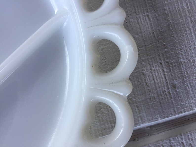 May include: White milk glass serving dish with a scalloped edge and four handles. The dish has a divided center.