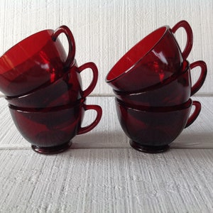 May include: Set of six red glass teacups stacked in two groups of three. The cups are a deep, rich red color and have a classic, rounded shape.
