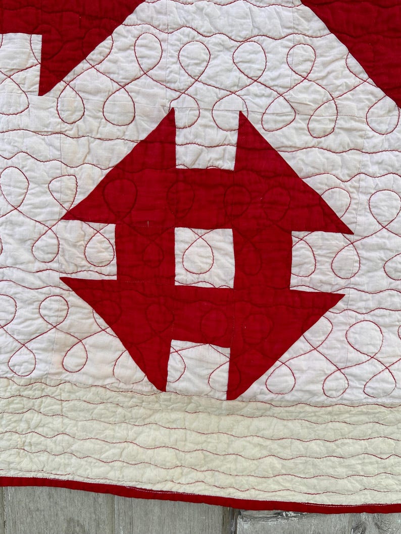 Peut inclure: Gros plan sur une courtepointe faite &agrave; la main avec un motif r&eacute;p&eacute;titif de formes rouges et blanches. La courtepointe pr&eacute;sente des motifs rouges en forme de fl&egrave;che et un fond blanc avec des coutures rouges en spirale. Le bord de la courtepointe est rouge.
