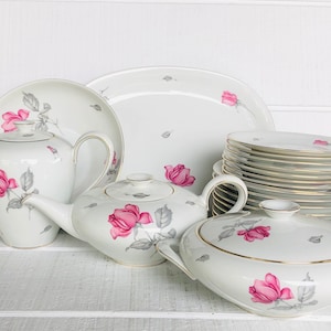 May include: A white porcelain tea set with a pink rose pattern. The set includes a teapot, creamer, sugar bowl, and a platter. The set is decorated with delicate pink roses and gray leaves.