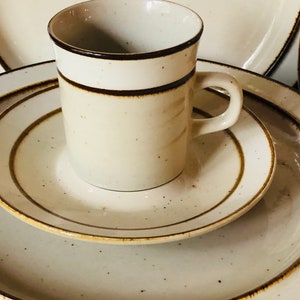 Może przedstawiać: Zestaw trzech ceramicznych talerzy z brązową obw&oacute;dką i beżową glazurą w kropki. Beżowy kubek z brązową obw&oacute;dką wok&oacute;ł g&oacute;rnej części znajduje się na talerzach.