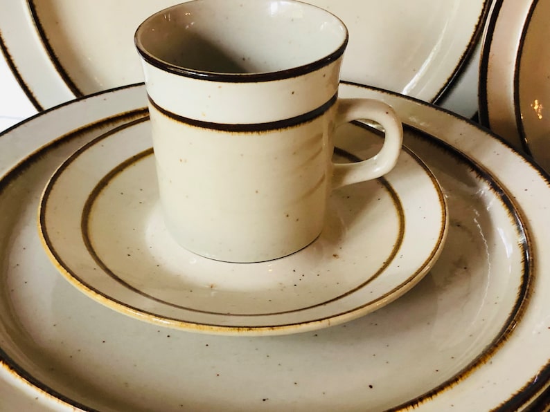 Może przedstawiać: Zestaw trzech ceramicznych talerzy z brązową obw&oacute;dką i beżową glazurą w kropki. Beżowy kubek z brązową obw&oacute;dką wok&oacute;ł g&oacute;rnej części znajduje się na talerzach.