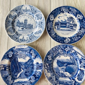 May include: Four blue and white decorative plates with scenic illustrations. One plate features text "LE VIEUX QUEBEC - OLD QUEBEC". The other plates depict landscapes and landmarks. Floral patterns border the plates.