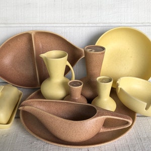 May include: A set of vintage ceramic kitchenware in yellow and brown speckled glaze. The set includes a butter dish, a gravy boat, a serving dish, a pitcher, and three small bowls.