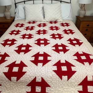 Peut inclure: Une courtepointe faite &agrave; la main avec un fond cr&egrave;me et un motif r&eacute;p&eacute;t&eacute; de formes g&eacute;om&eacute;triques rouges. La courtepointe est sur un lit avec des oreillers blancs et une t&ecirc;te de lit en m&eacute;tal noir. Le design de la courtepointe est un contraste saisissant de couleurs et de formes.