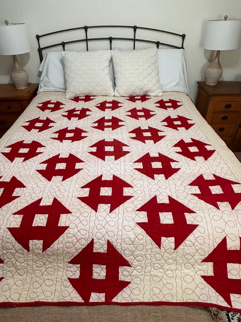 Peut inclure: Une courtepointe faite &agrave; la main avec un fond cr&egrave;me et un motif r&eacute;p&eacute;t&eacute; de formes g&eacute;om&eacute;triques rouges. La courtepointe est sur un lit avec des oreillers blancs et une t&ecirc;te de lit en m&eacute;tal noir. Le design de la courtepointe est un contraste saisissant de couleurs et de formes.