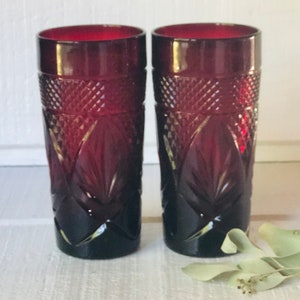 May include: Two ruby red glass tumblers with a diamond pattern. The glasses are clear and have a vintage look.