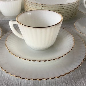 May include: A set of white milk glass teacups and saucers with a gold trim. The cups and saucers have a fluted design.